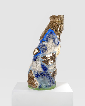 A colourful, irregularly shaped sculpture with metallic sections. There is an eye-like shape on the left-hand side and several shiny metallic sections which look similar to fish scales or bird feathers. 