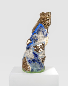 A colourful, irregularly shaped sculpture with metallic sections. There is an eye-like shape on the left-hand side and several shiny metallic sections which look similar to fish scales or bird feathers. 