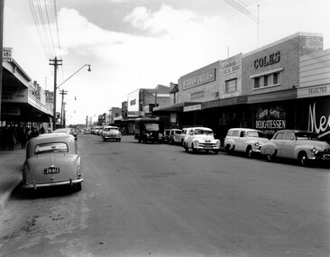 The shopping strip along Centre Bentleigh, with cars travelling along the road and plenty more parked 
