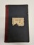 Green, hard cover minute book with red leather binding on the spine.