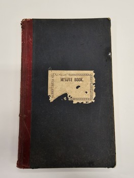 Green, hard cover minute book with red leather binding on the spine.