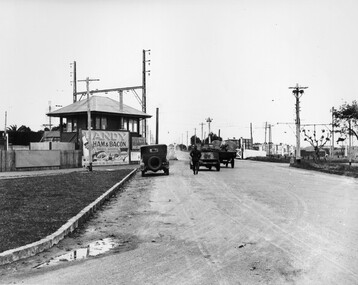 Cars travelling along an unsealed road and over the level crossing at Moorabbin