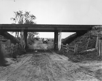 A muddy, unsealed road passes under a railway bridge