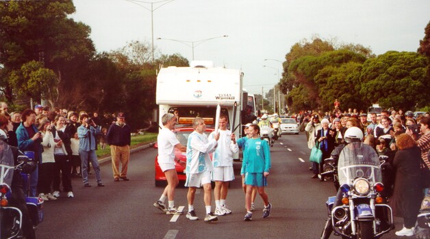 Participants in the torch relay exchange the torch while a large crowd looks on