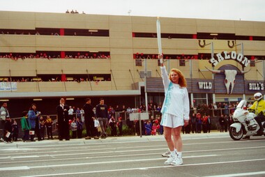 A woman, dressed in the uniform of an Olympic torch bearer, holds the torch aloft 