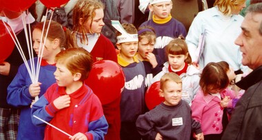 A crowd of children, some holding red balloons, attend the Olympic torch relay