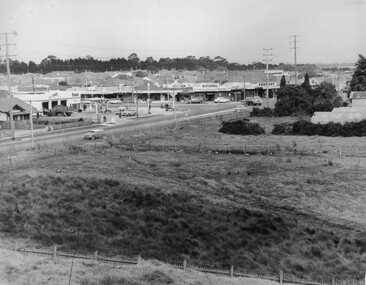 A view over paddocks toward a shopping strip situated in front of a residential area