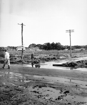 People trying to navigate enormous puddles along the street and at the intersection of unsealed roads