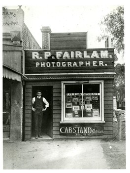 A man dressed in a suit stands in the doorway of a wooden building