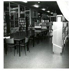 A library interior, with tables and chairs surrounded by bookshelves