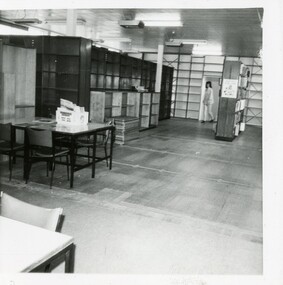 A view of the library interior with empty shelving and a woman walking through a doorway