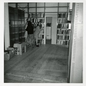 Three women unpacking books onto empty shelves. One is facing the camera