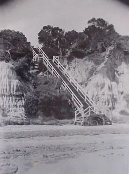 A steep wooden staircase leads down to the beach from the clifftop above