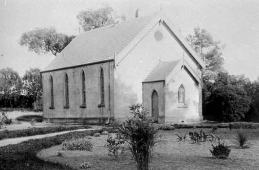 A small church building with four narrow windows along the left-hand side, surrounded by lawn and plants. 