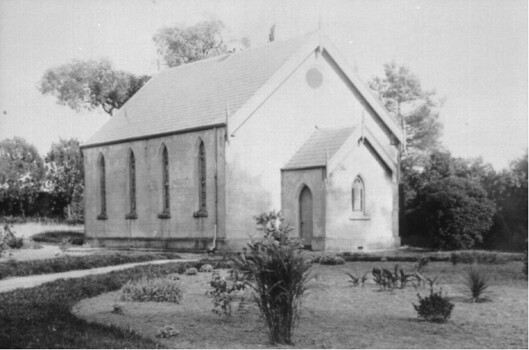 A small church building with four narrow windows along the left-hand side, surrounded by lawn and plants. 