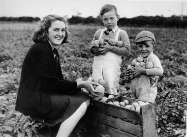 Image shows a young woman and two small boys holding potatoes in a field