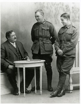 Three men, one seated, two standing, looking at one another