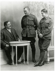 Three men, one seated, two standing, looking at one another