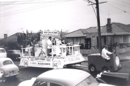 Large float being driven down a busy street, past homes and vehicles