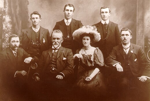 A man and woman sitting side-by-side in the centre, surrounded by five men