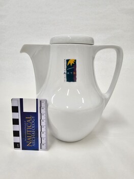 Small white coffee pot with purple, green and yellow Moorabbin Arts Centre Logo with small Nautical Archaeology scale to 8cm placed against left side