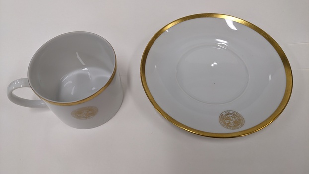 White cup and saucer with gold edging and City of Moorabbin logo, separated