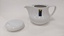 Small white coffee pot with purple, green and yellow Moorabbin Arts Centre Logo with lid removed and placed to left