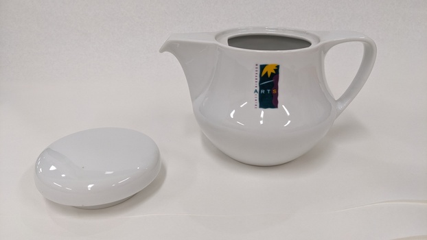 Small white coffee pot with purple, green and yellow Moorabbin Arts Centre Logo with lid removed and placed to left