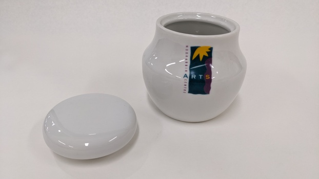 Small white sugar bowl with purple, green and yellow Moorabbin Arts Centre Logo with lid removed and placed to left