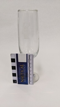 Glass champagne flute with white Kingston Arts logo, including scale to 8cm leaning against glass