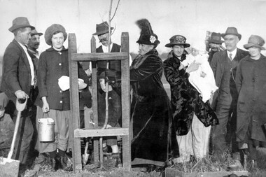 A group of people standing behind a freshly planted tree sapling