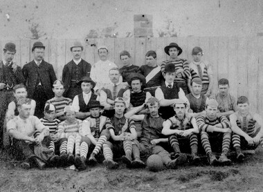 Group photo of men who have recently played a game of football, most in uniform, some in street wear