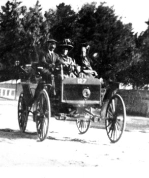A man and two women driving in an early car