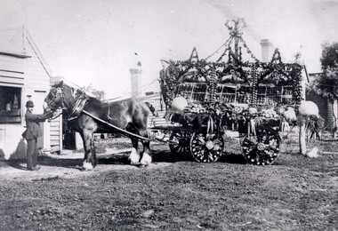 A man in a bowler hat is holding the reins of a horse that is attached to a decorated wagon.