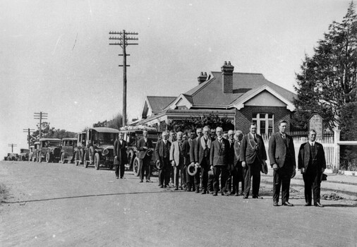 A group of men standing in two lines ahead of a convey of cars, forming a funeral procession