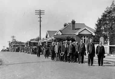 A group of men standing in two lines ahead of a convey of cars, forming a funeral procession