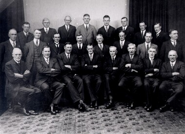 Three rows of men dressed in suits. The front row is seated and the remaining two rows are standing.