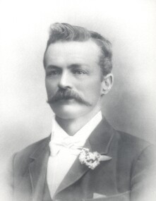 A man looking to the side of camera, dressed in a suit with a floral boutonniere