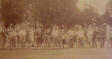 A group of men standing in a row each with a bicycle by their side.