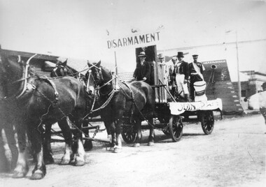 A group of men are standing on a wagon attached to four horses. The wagon has a banner across with the word 'disarmanent' on it.