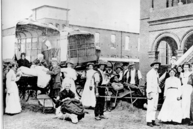 Black and white image of men and women patients arriving at the benevolent asylum with the steps to the building in the background and patients being carried on stretchers from trucks into the centre