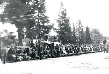 Black and white image of men and women sitting on the back of a train in open air carriages