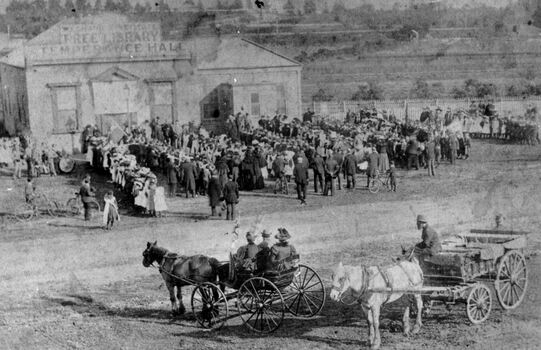 Black and white image of people gathering outside the Mechanics Hall, Temperance Hall and Free Library, Nepean Highway, Cheltenham - in background the railway line and paddocks