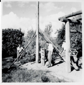 Three men working on a tall wooden structure with a central tall pole.