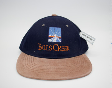 Blue baseball cap with tan colours peak and falls creek embroidered on front in similar colour as peak