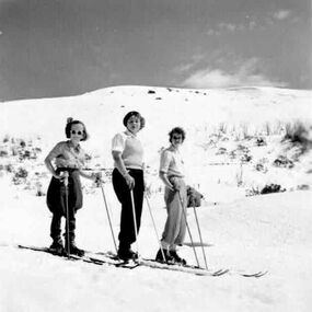 Three women on skies with snow covered slopes in background