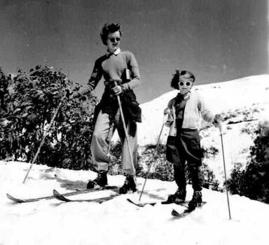 A woman and a child on skies. Snow covered slopes in background