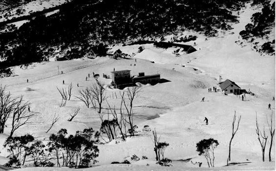 Aerial view including Lodge in the centre between snow covered slopes and trees.