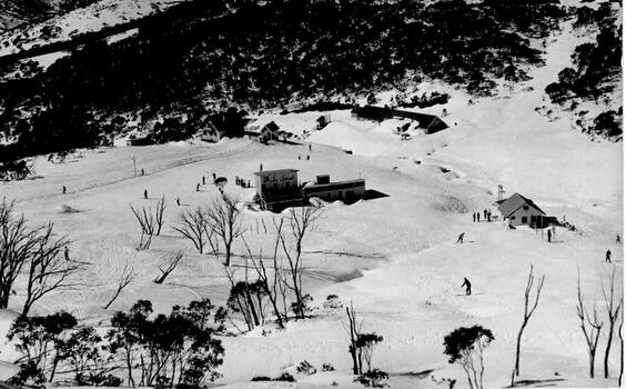 Aerial view including Lodge in the centre between snow covered slopes and trees.