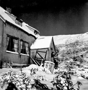 Albury Ski Club Lodge surrounded by snow. 2 people are standing in front of the doorway.